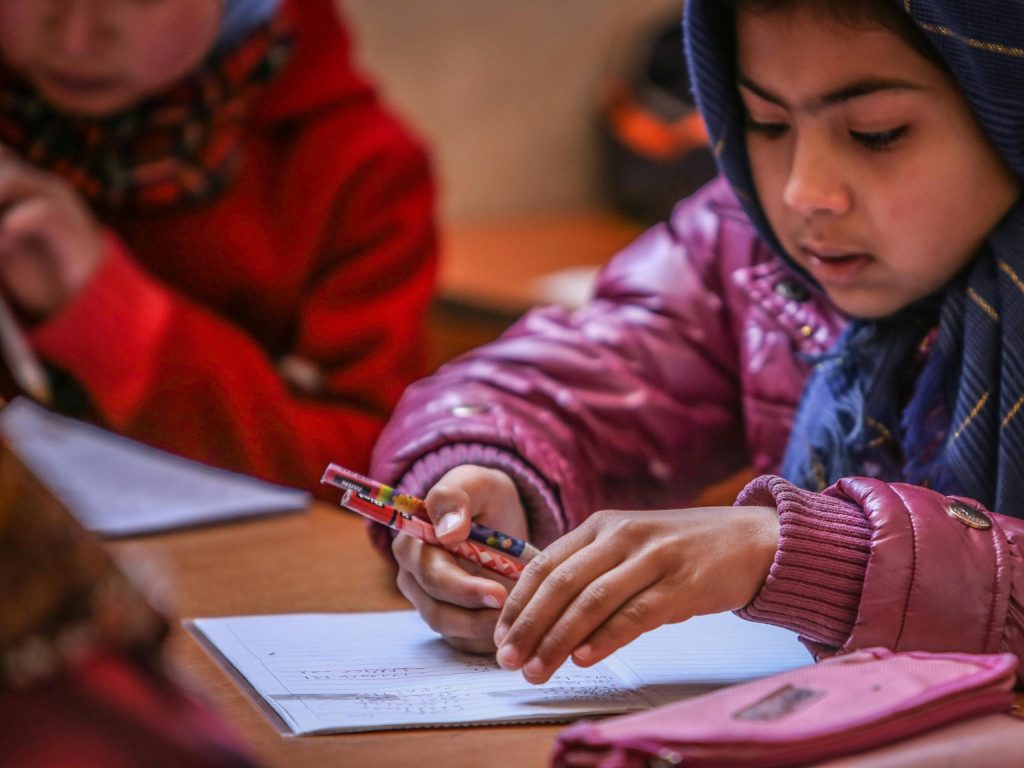 Young Afghan students engaged in learning at a classroom desk.
